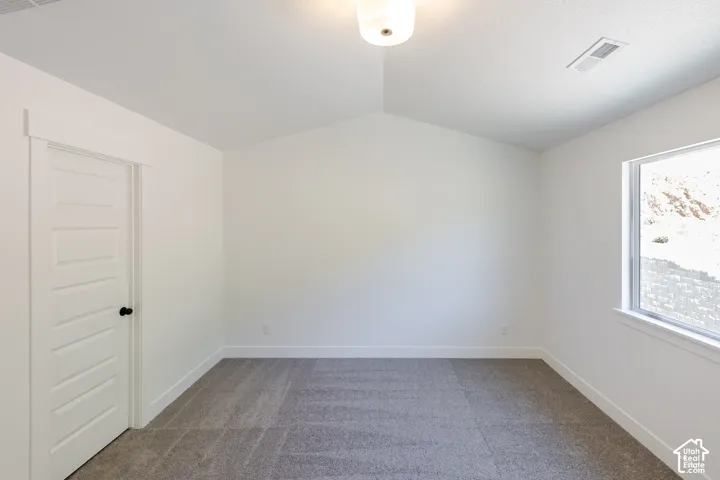 Vaulted ceiling, neutral carpet, white trim, recessed window, and a paneled interior door