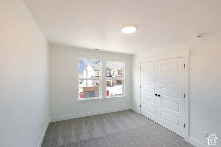 White walls with carpet flooring, complemented by two windows with white trim, a flush mount ceiling light, and a two-door closet with paneling and dark hardware