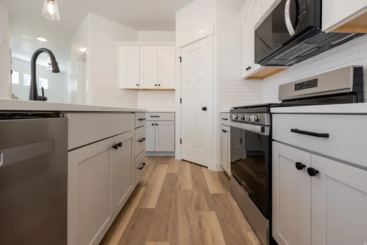 White shaker-style cabinetry, stainless steel appliances, wood-finish flooring, subway tile backsplash, and a black matte faucet