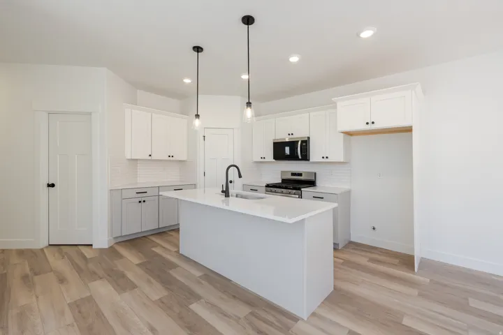 Kitchen featuring white upper cabinetry, light gray lower cabinetry, a center island with countertop, stainless steel appliances, and wood-finish flooring