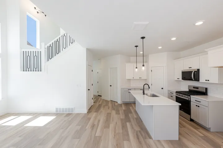 Open-concept living space with wood-finish flooring, a contemporary kitchen, white cabinetry, a center island with a sink, and a black appliance package