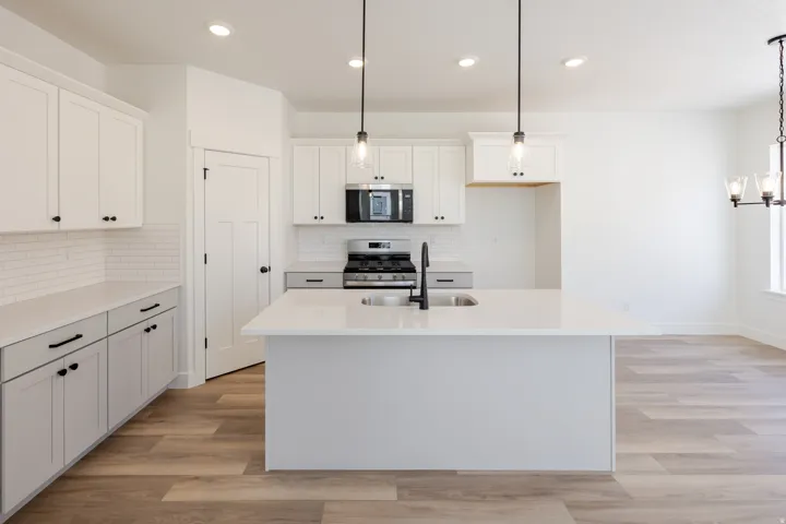 Kitchen featuring a central island with an integrated sink, white shaker cabinetry, subway tile backsplash, and wood-finish flooring