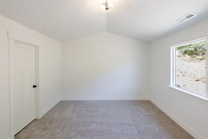 Vaulted ceiling, neutral carpet flooring, white interior door with black hardware, and a single window with white trim