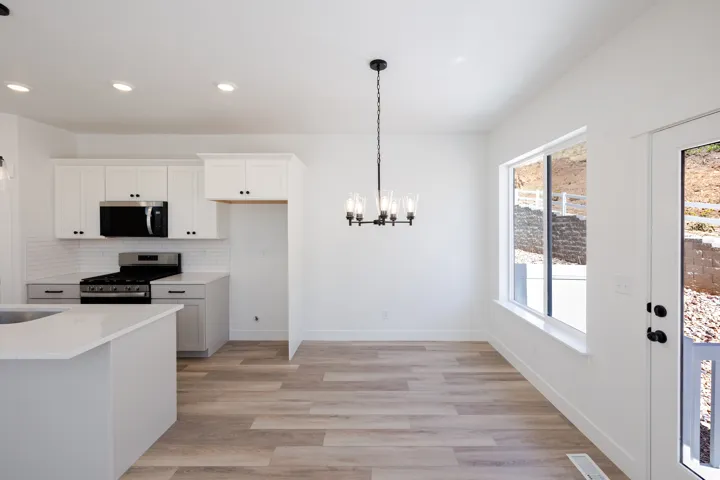 Kitchen and dining area featuring white cabinetry, stainless steel appliances, wood-finish flooring, a contemporary chandelier, and a large window