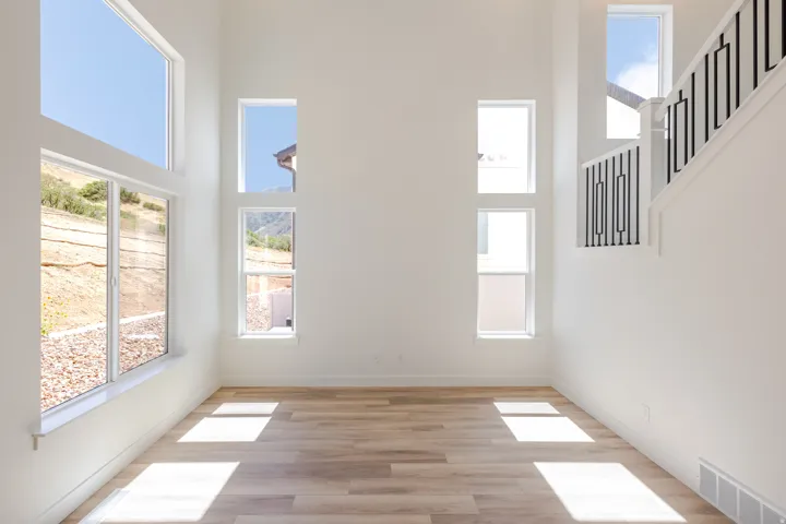 Soaring ceilings, abundant natural light, wood-finish flooring, white walls, and a staircase with a black metal railing