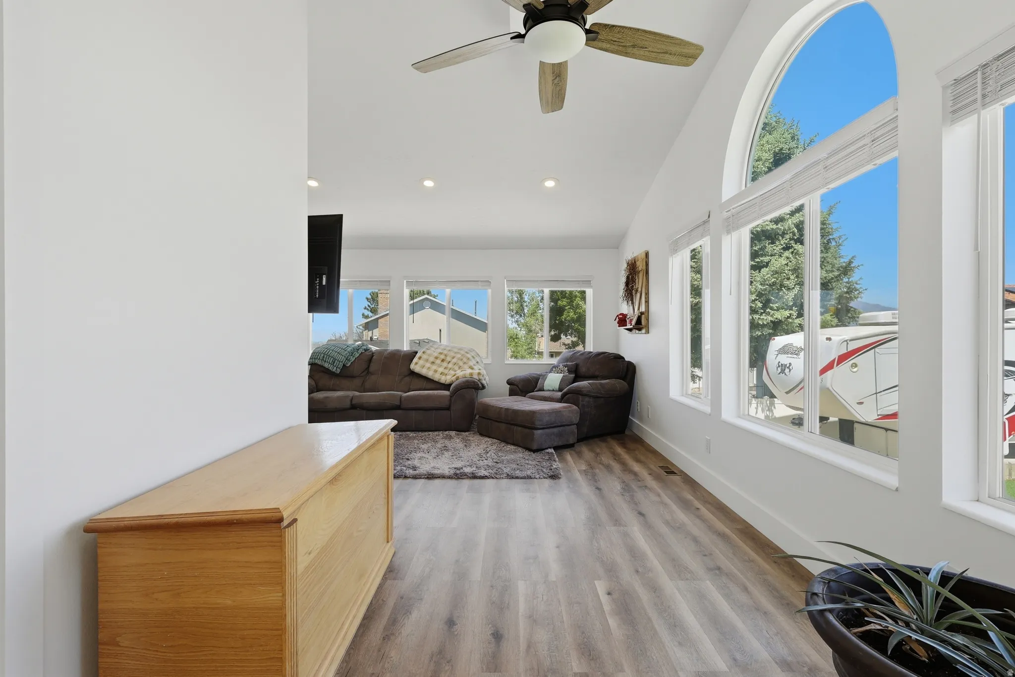 Living area featuring wood-finish flooring, vaulted ceilings with a ceiling fan, recessed lighting, and multiple windows including an arched accent window