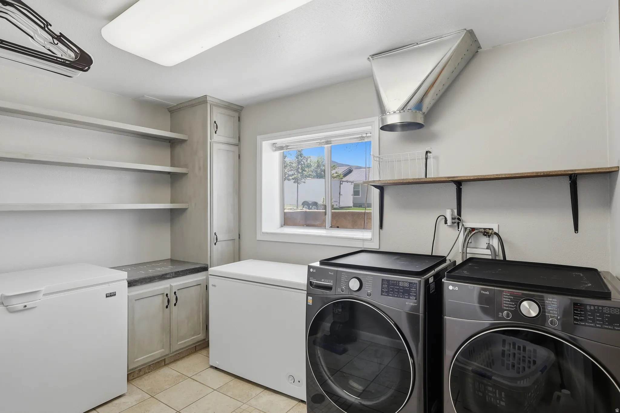Dedicated utility room with ample storage, featuring light-toned cabinetry, open shelving, and a built-in countertop