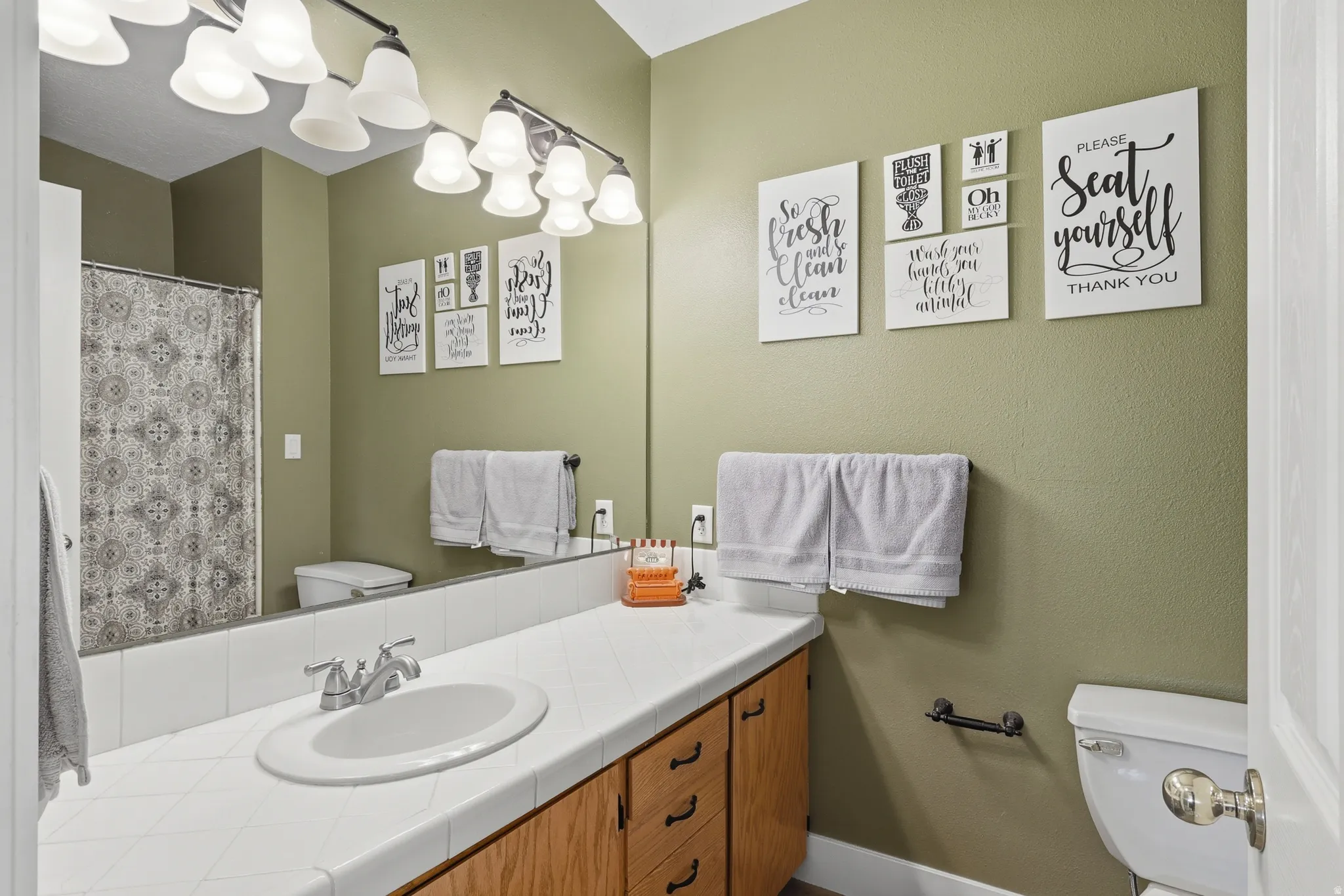 Bathroom featuring a single vanity with an integrated sink, tile countertop, and wood-finish cabinetry