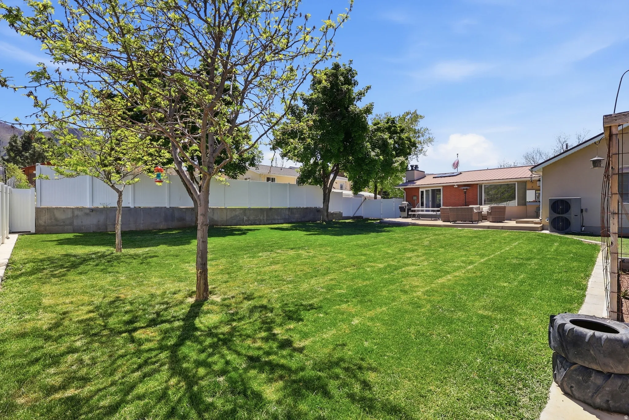 Expansive backyard featuring a manicured lawn, established trees, and a white privacy fence