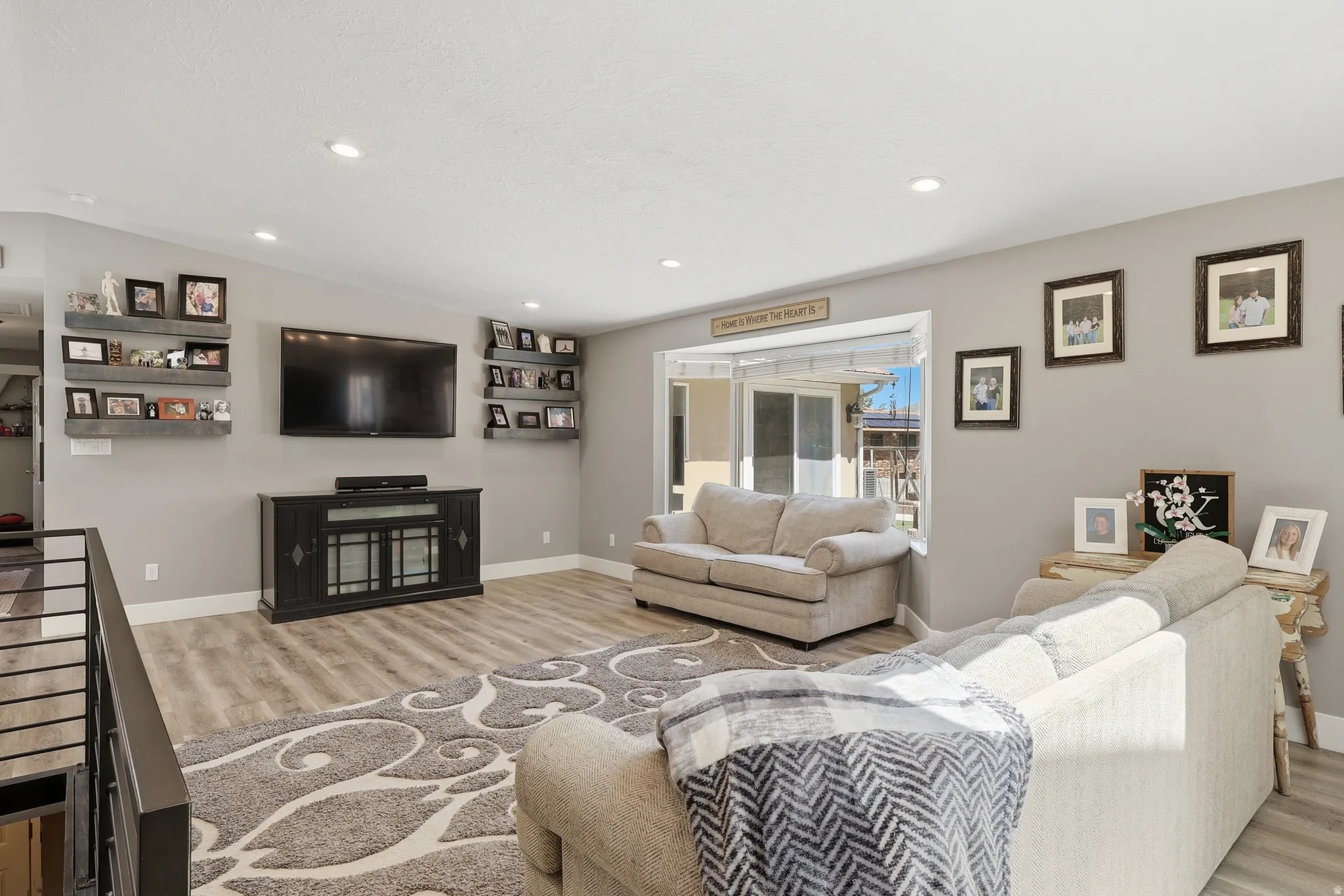 Open-concept living space featuring wood-finish flooring, recessed lighting, a bay window, and a built-in media console
