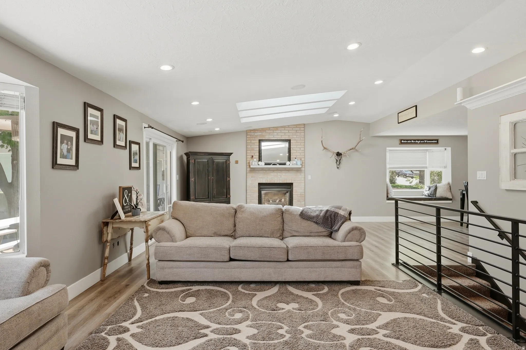 Spacious living area featuring a brick fireplace with mantel, sloped ceiling with skylights, recessed lighting, and wood-finish flooring