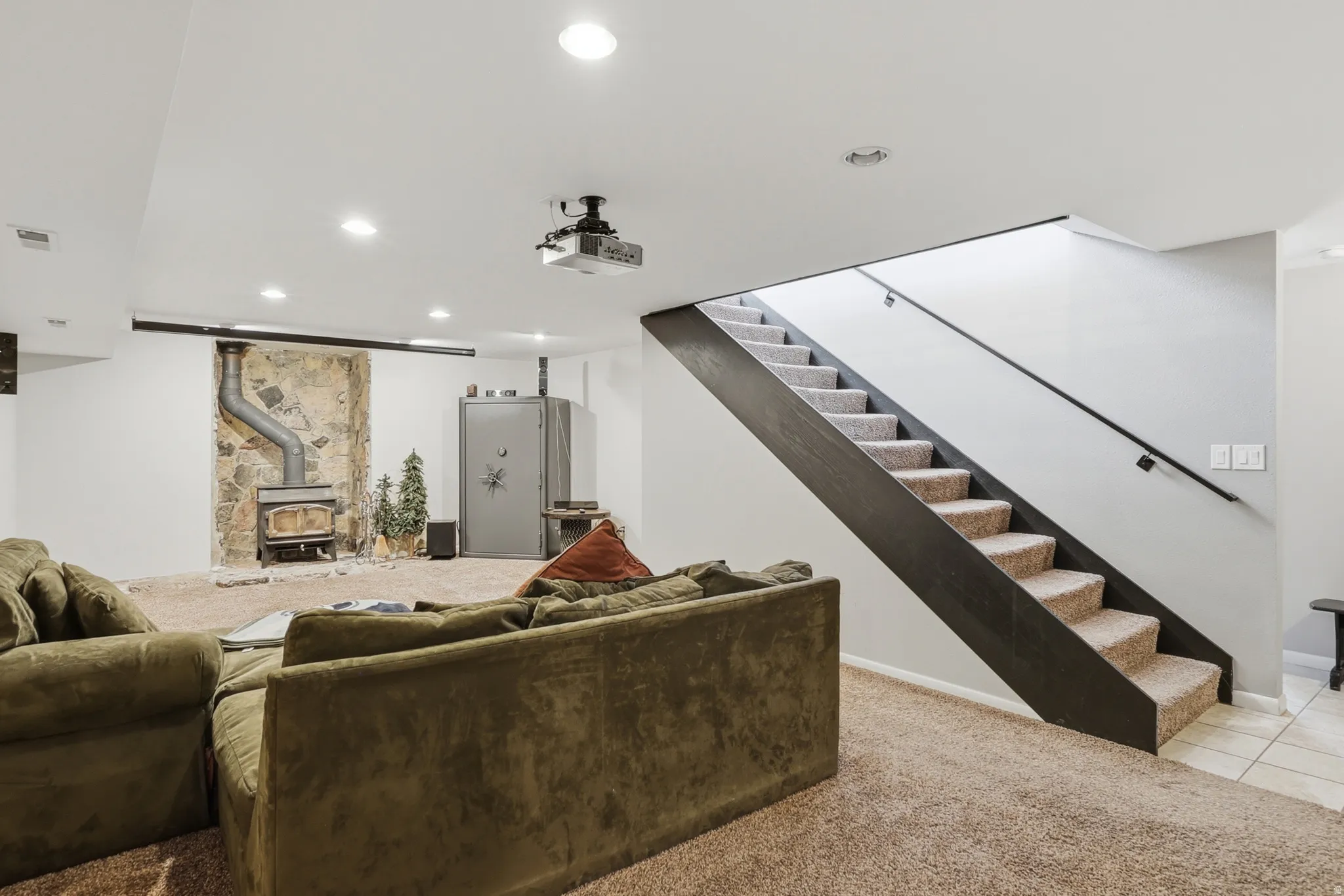 Finished lower level featuring a carpeted recreation area, stone accent wall with a wood-burning stove, and recessed lighting