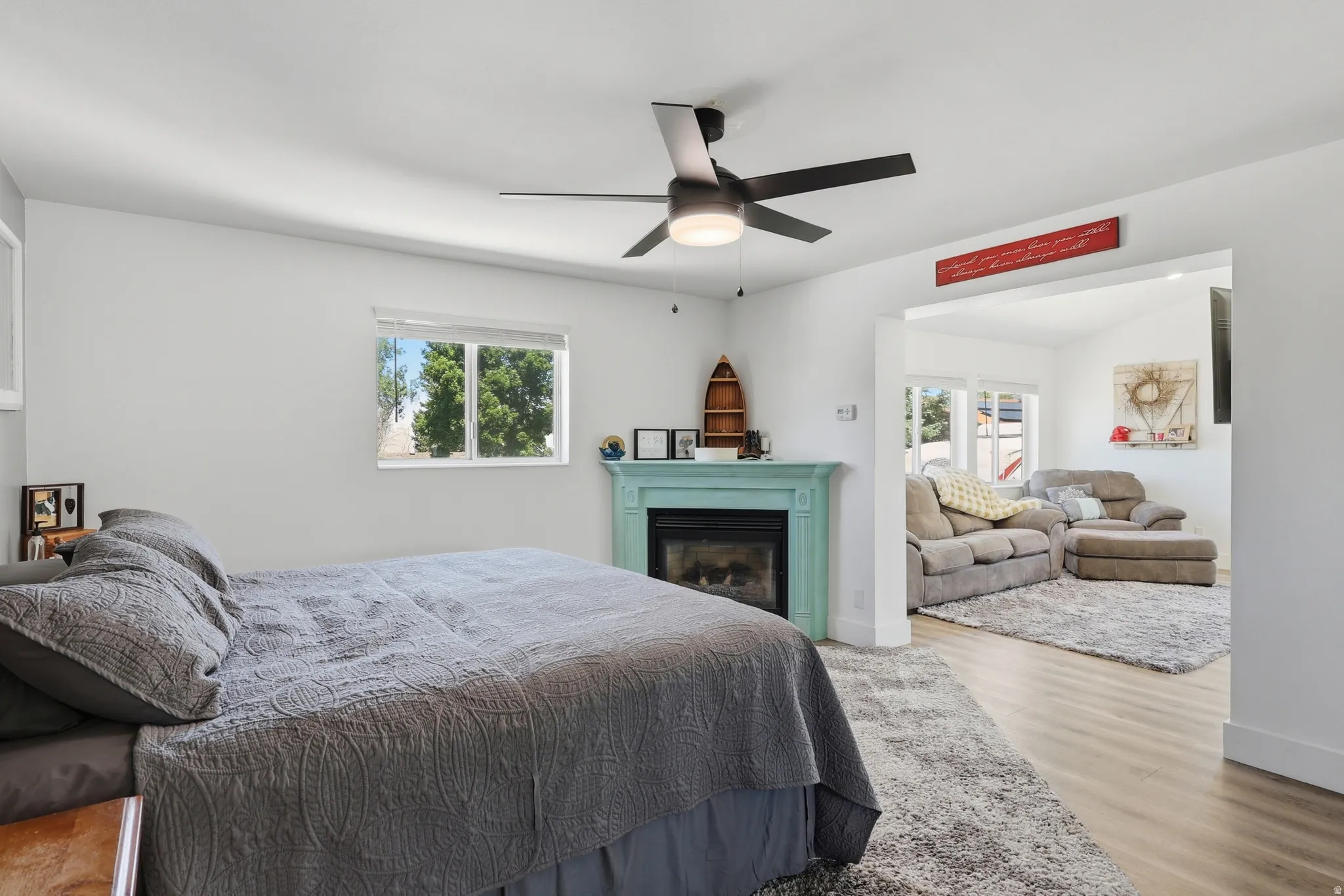 Bedroom featuring a decorative fireplace with a light blue mantel, a ceiling fan with integrated lighting, and a window providing natural light