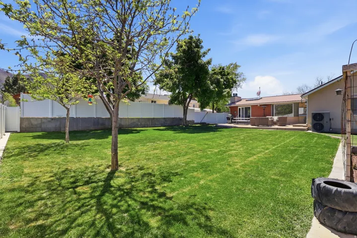Expansive backyard featuring a manicured lawn, established trees, and a white privacy fence