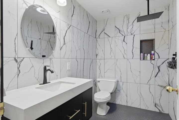 Contemporary bathroom featuring large format marble-look wall tiling, a rectangular vessel sink with a matte black faucet, and a wall-mounted matte black rainfall showerhead