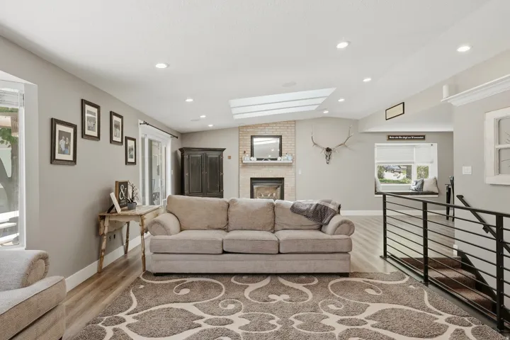 Spacious living area featuring a brick fireplace with mantel, sloped ceiling with skylights, recessed lighting, and wood-finish flooring