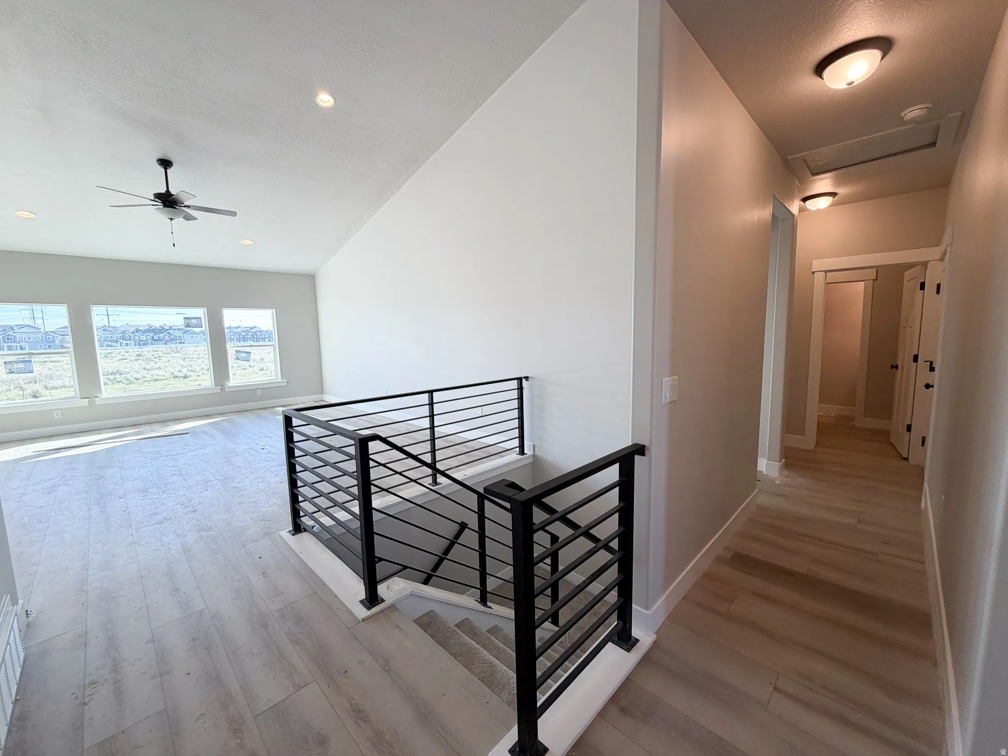 Open living space featuring wood-finish flooring, a contemporary black metal railing, and a vaulted ceiling with a ceiling fan