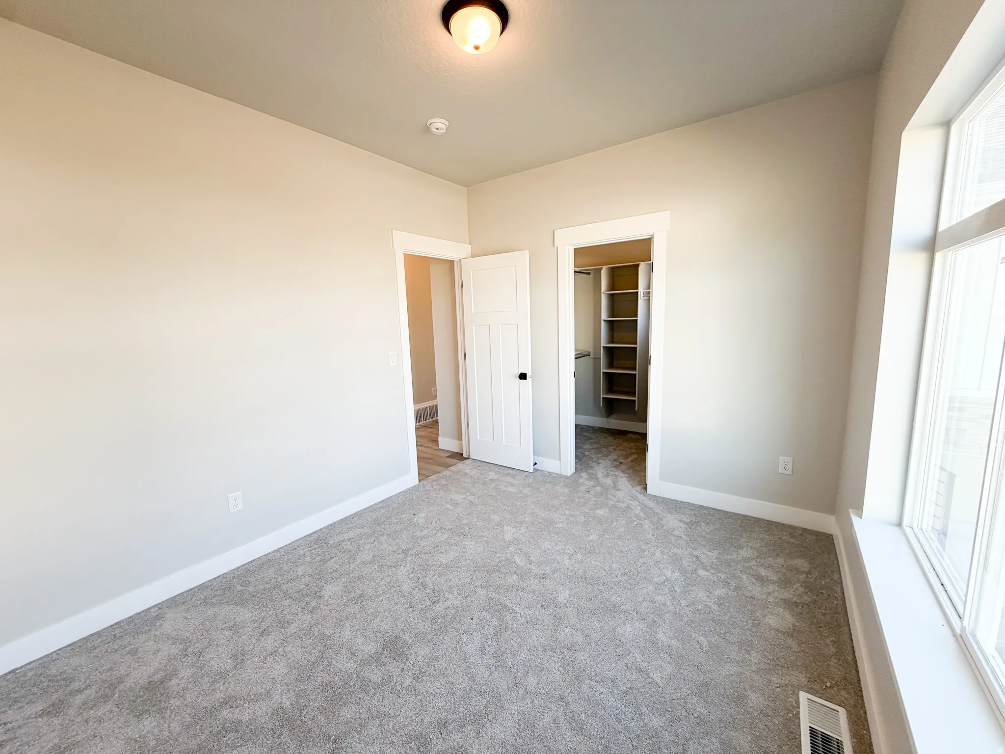 Carpeted room featuring neutral wall tones, a large window with white trim, a built-in closet with shelving, and a panel door