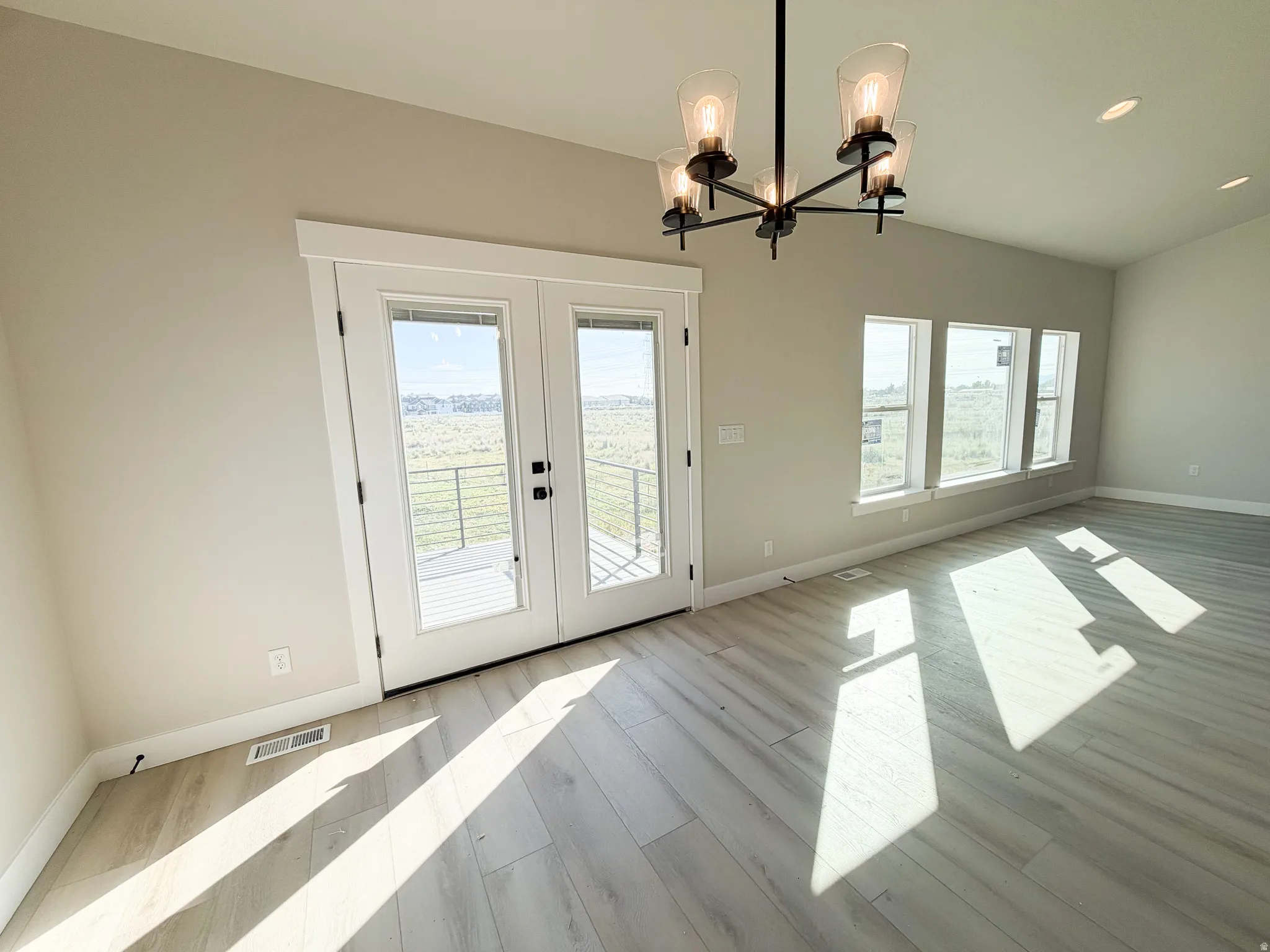 Spacious room featuring a black chandelier with clear glass shades, wood-finish flooring, recessed lighting, and a double patio door