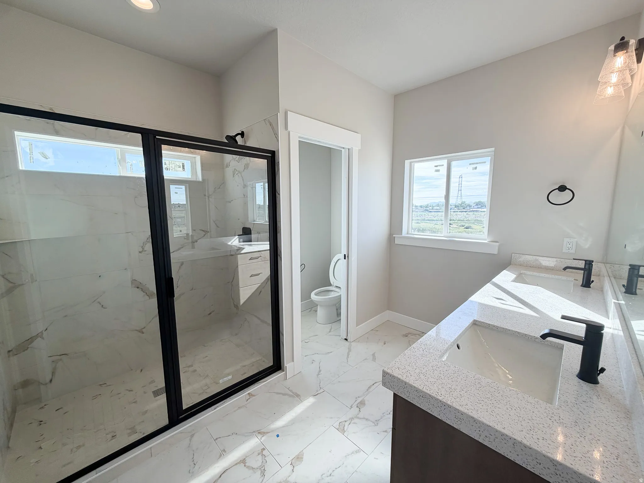 Contemporary bathroom featuring a spacious walk-in shower with black-framed glass enclosure, dual vanity with undermount sinks, speckled countertops, and matte black fixtures