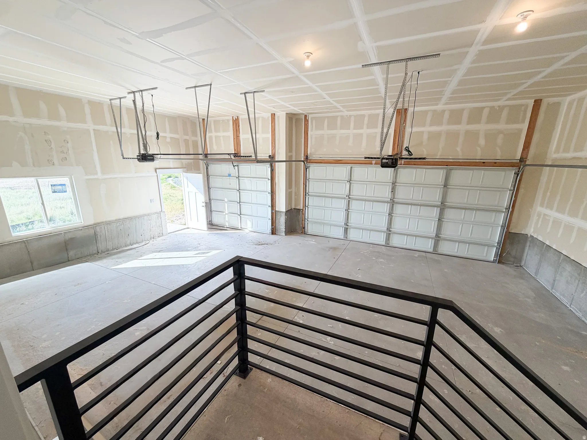 Spacious garage featuring three overhead doors with automatic openers, concrete flooring, and an additional access door