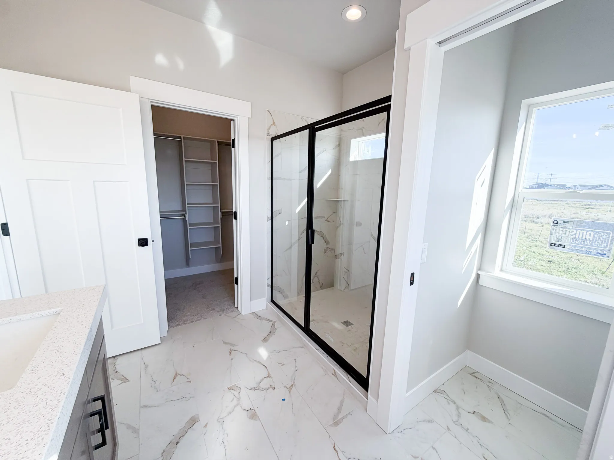 Contemporary bathroom featuring large format tile flooring, a walk-in shower with black-framed glass enclosure, and a built-in vanity with an undermount sink and light-toned countertop