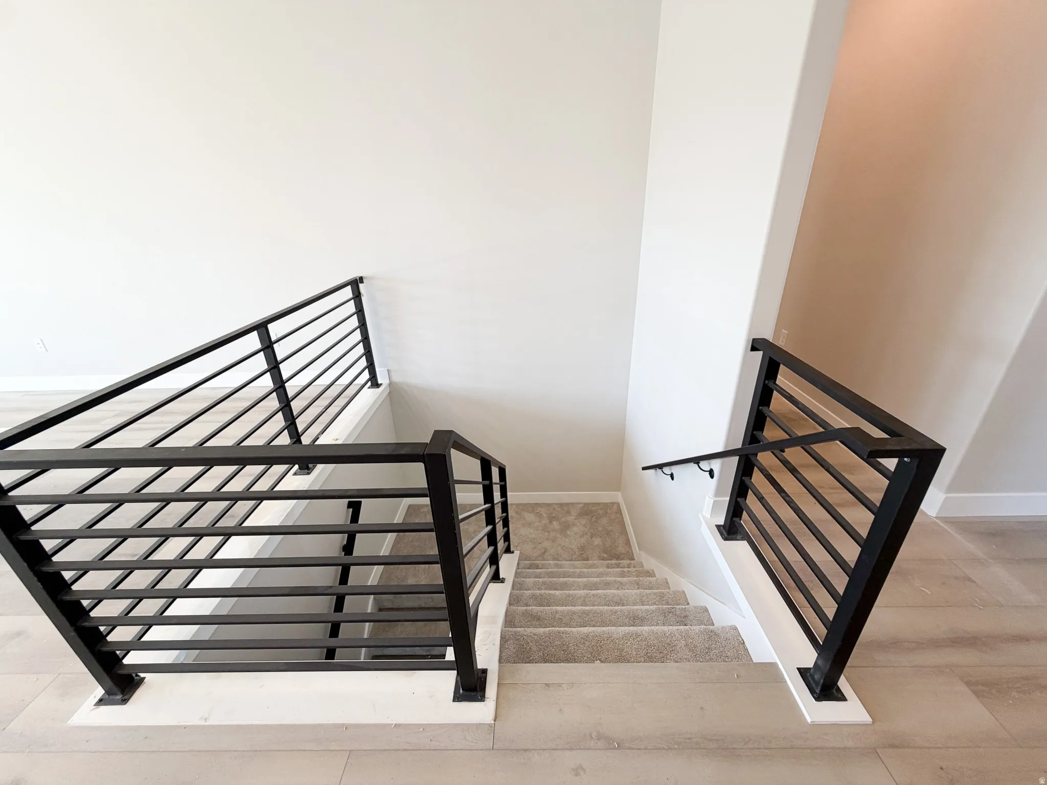 Contemporary staircase featuring horizontal black metal railings and a coordinating wall-mounted handrail