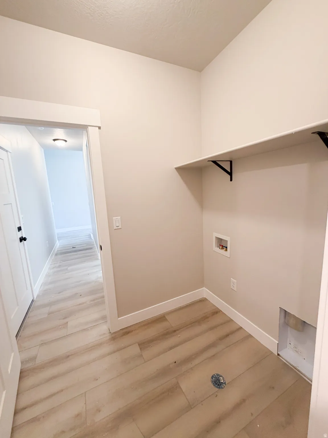Dedicated utility space featuring wood-finish flooring, light neutral wall paint, and a built-in wall shelf with black support brackets
