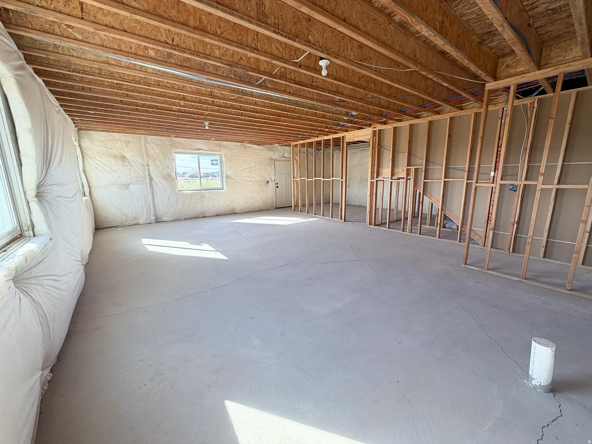 Unfinished basement offering expansive concrete flooring, exposed wood joists, framed interior walls, and multiple windows providing natural illumination