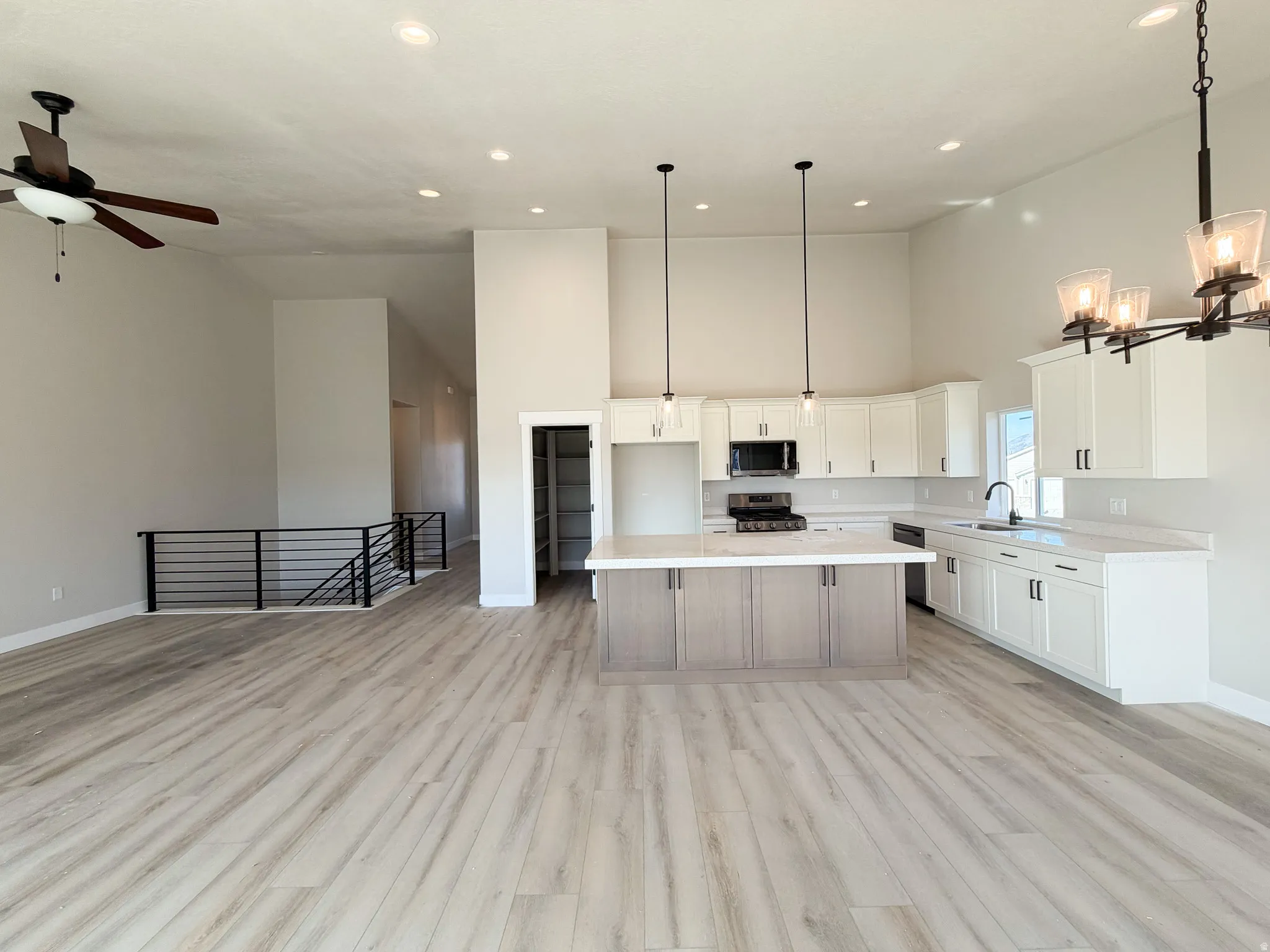 Spacious open-concept kitchen and living area featuring wood-finish flooring, high ceilings with recessed lighting, and a modern kitchen with a large island and white cabinetry