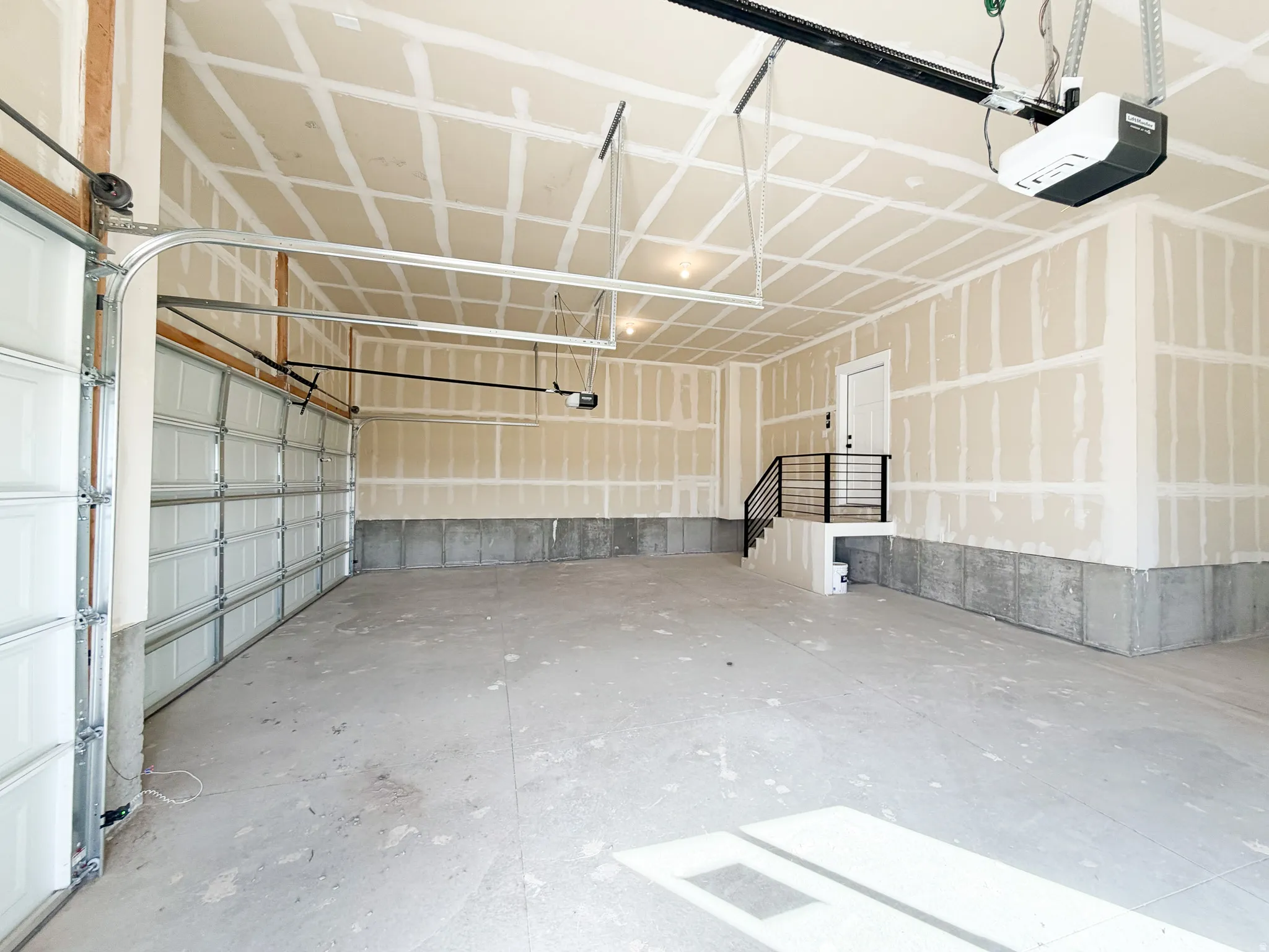 Spacious two-car garage featuring a concrete floor, automatic garage door opener, and interior access door with black metal railing