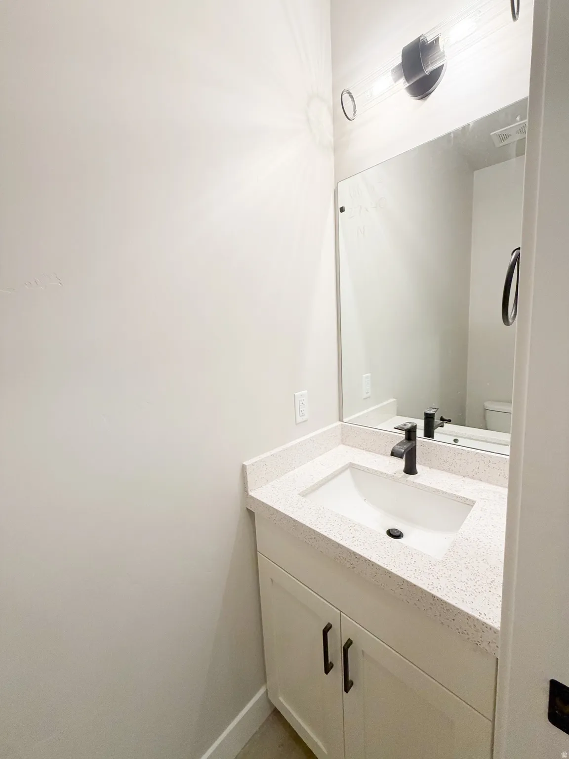 White vanity with shaker-style cabinetry, a light speckled countertop, and an undermount sink