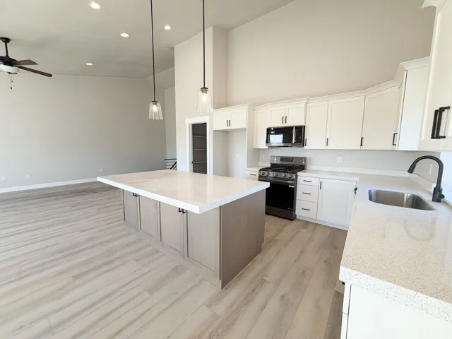 Spacious kitchen featuring an expansive island with a light-toned wood-finish base and a light-toned countertop, complemented by white cabinetry and stainless steel appliances