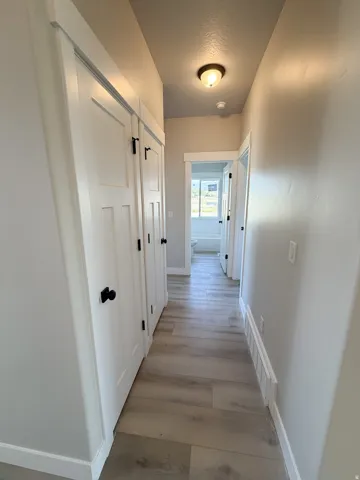 Hallway featuring wood-finish flooring, white paneled doors with black hardware, and light neutral wall tones