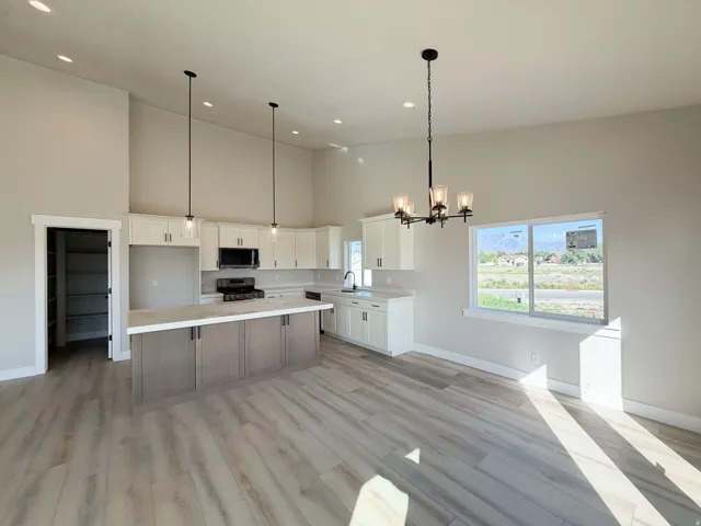 Open-concept kitchen and dining area featuring a central island with a light-toned countertop, white cabinetry with dark hardware, and wood-finish flooring