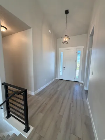 Entryway featuring light wood-finish flooring, vaulted ceiling, and a modern geometric pendant light