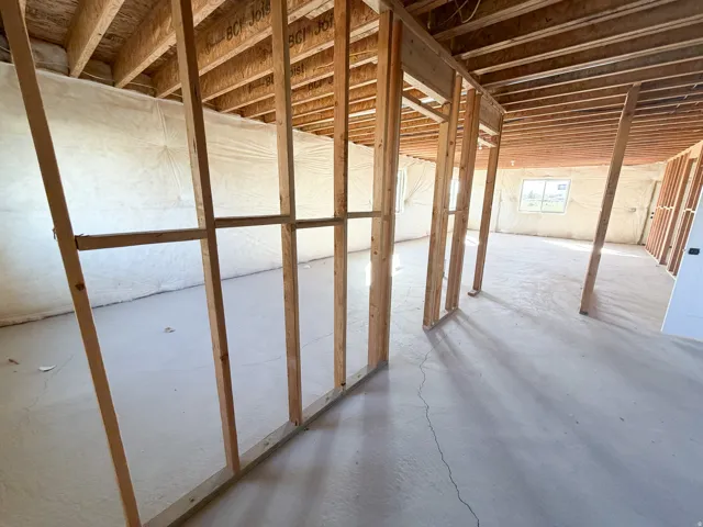 Unfinished interior space featuring exposed wooden framing, an open ceiling with visible joists, and a poured concrete floor