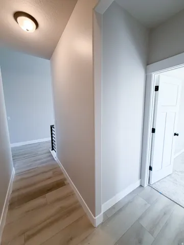 Hallway with wood-finish flooring, light gray wall paint, and white baseboards