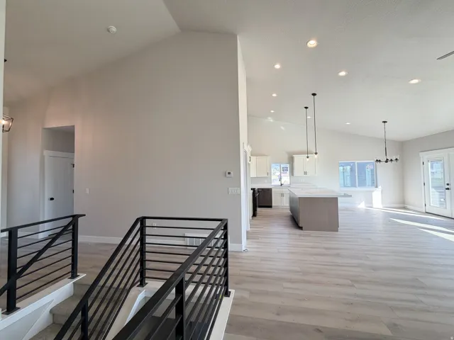 Vaulted ceilings enhance this open-concept interior featuring light wood-finish flooring, a modern black metal staircase railing, recessed lighting, and a kitchen island with pendant lighting