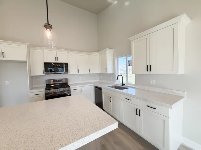 Kitchen featuring a spacious island with a light-toned countertop, white cabinetry with matte black hardware, stainless steel range with overhead microwave, and a black gooseneck faucet above the sink