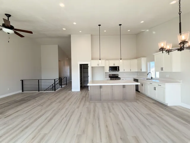 Spacious open-concept kitchen and living area featuring wood-finish flooring, high ceilings with recessed lighting, and a modern kitchen with a large island and white cabinetry