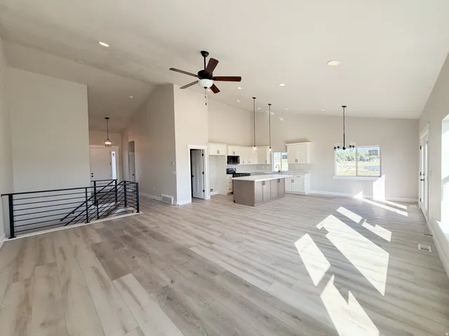 Spacious open-concept living area featuring high vaulted ceilings, light wood-finish flooring, and a modern kitchen with a large island