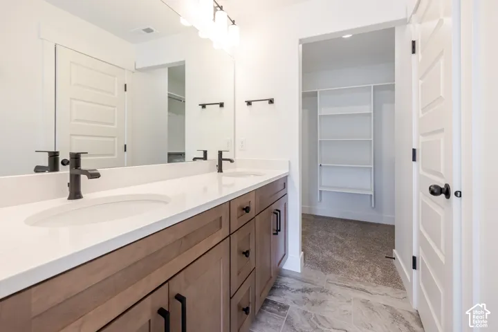 Dual vanity with integrated sinks, light-toned countertop, wood-finish cabinetry with dark hardware, tile flooring, and integrated shelving in the alcove
