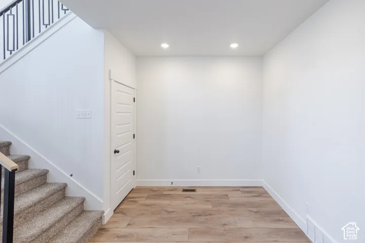 Neutral white walls, wood-finish flooring, recessed ceiling lighting, louvered panel door, and carpeted stairs with a metal and wood railing