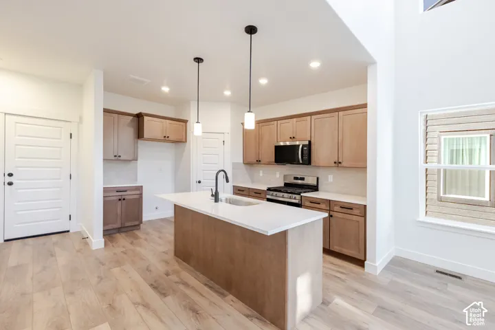 Kitchen featuring a central island with a sink, stainless steel appliances, wood-finish flooring, recessed lighting, and a high ceiling