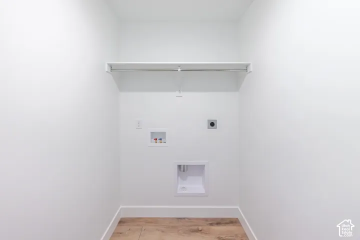 Interior laundry utility space featuring wood-finish flooring, white walls, a built-in shelf with hanging rod, and dedicated appliance hookups