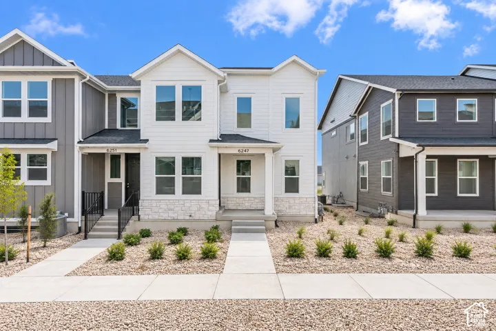 Modern townhome exterior with light siding, dark-framed windows, a covered entry, and a stone accent foundation