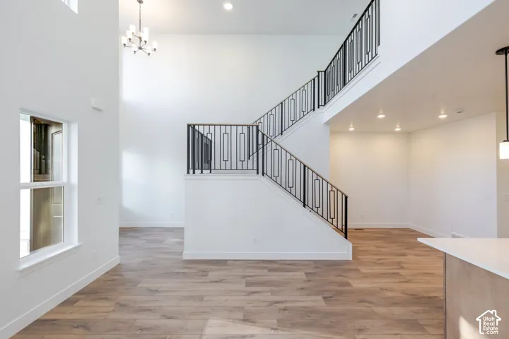 Two-story entryway with wood-finish flooring, a modern chandelier, and an open staircase featuring black iron railings