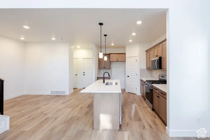 Kitchen with wood-finish flooring, recessed lighting, a central island with a sink, stainless steel appliances, and wood cabinetry