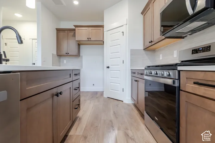 Kitchen featuring wood-finish cabinetry, stainless steel appliances, light-toned countertops, tile backsplash, and light wood-finish flooring